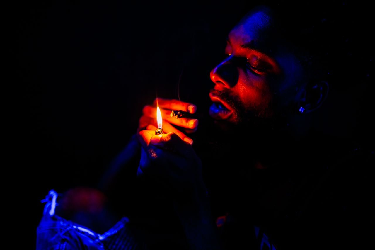 A man illuminated by a flame, creating a dramatic contrast in a nighttime setting.